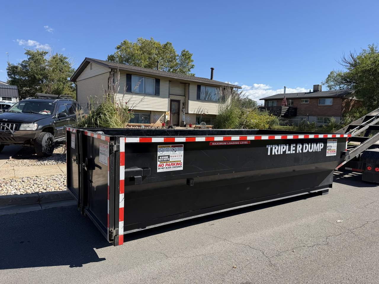 Close-up of a Triple R Dump roll-off dumpster at the curb in Clinton, Utah, with its maximum loading level sticker