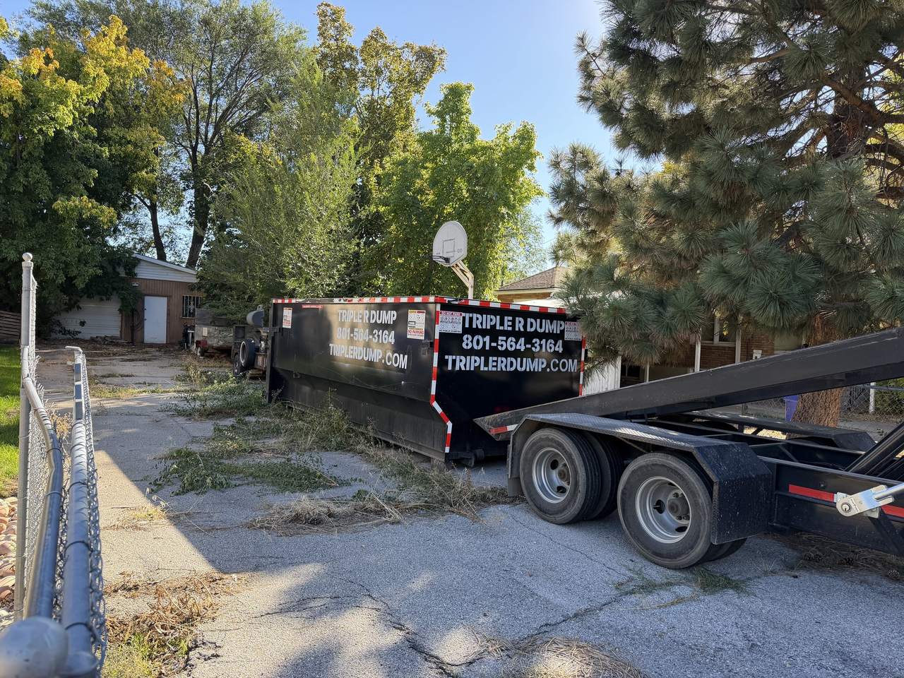 Triple R Dump roll-off dumpster on an old concrete drive beside a detached garage in Bountiful, Utah