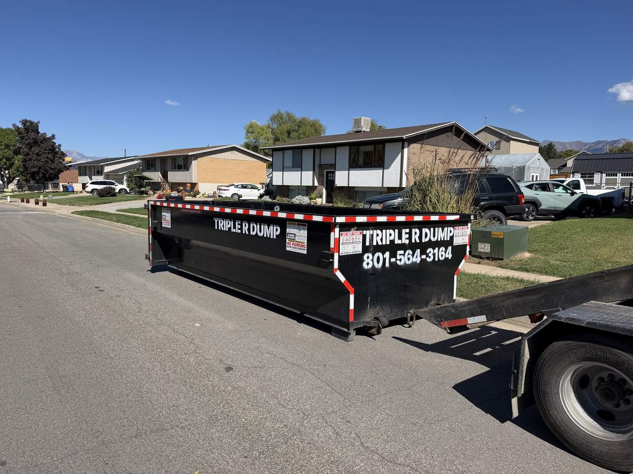Triple R Dump roll-off truck setting a dumpster on a Clinton, Utah street lined with split-level homes