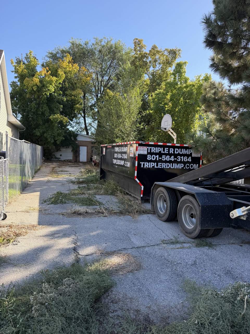 Roll-off trailer in front of a Triple R Dump dumpster on a long concrete driveway in Bountiful, Utah