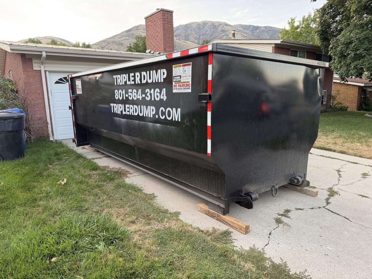 Close-up of a Triple R Dump roll-off dumpster sitting on wood boards on a Brigham City, Utah driveway
