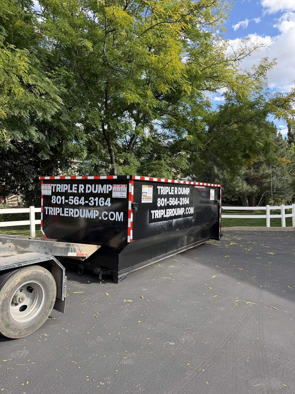 Triple R Dump roll-off dumpster on asphalt beside a white fence in North Ogden, Utah